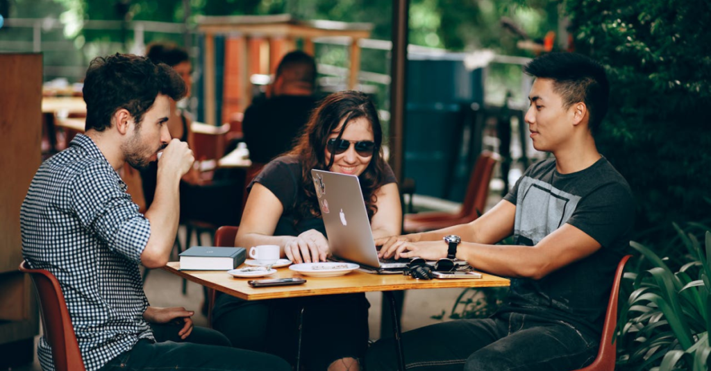 3 jovens sentados em mesa de café conversando