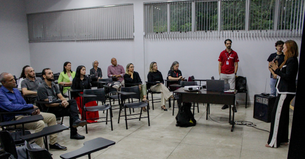 pessoas sentadas em uma sala observando outra pessoa falando à frente